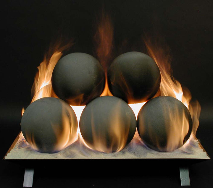 Five matte black spherical objects resting on a metal tray, surrounded by visible flames against a dark background.